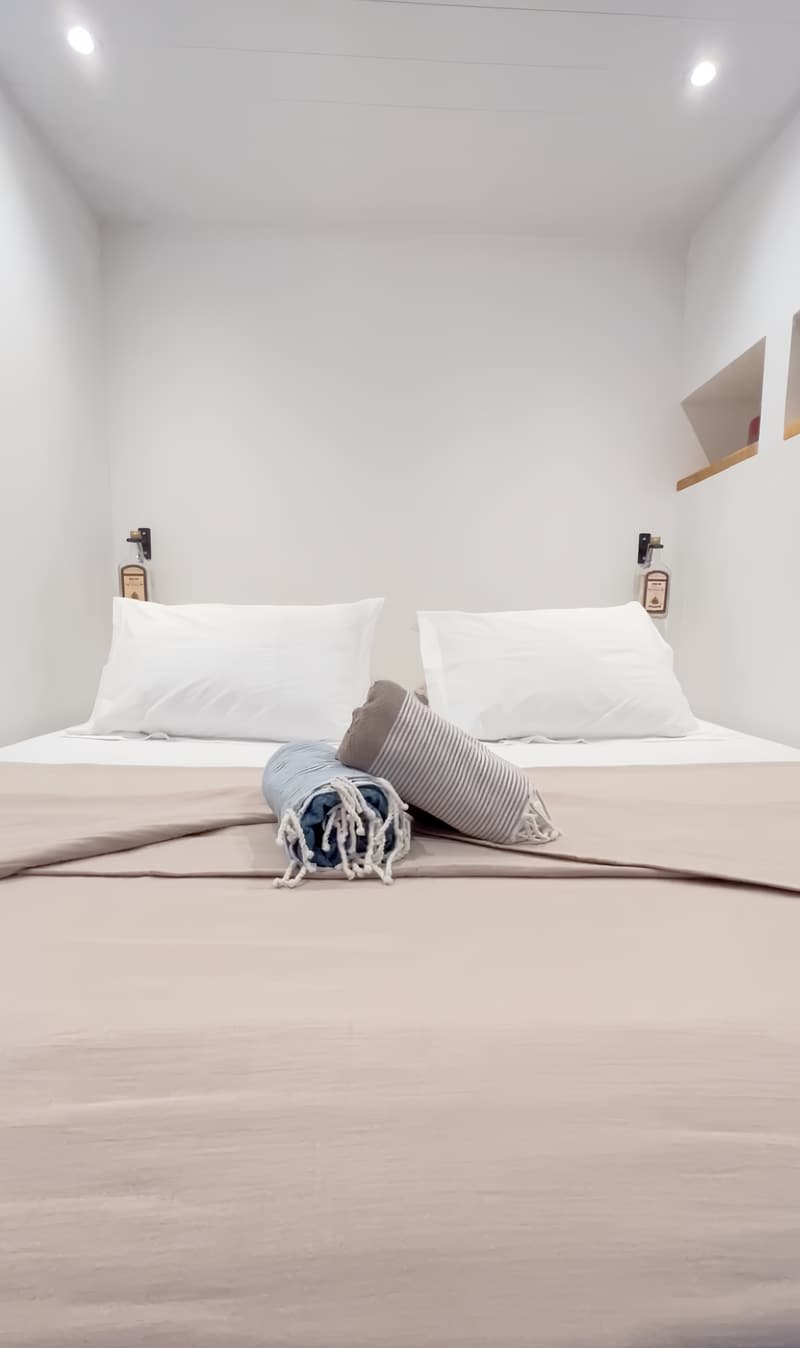 La chambre : le lit king size aux draps blancs, deux oreillers et des foutas roulées