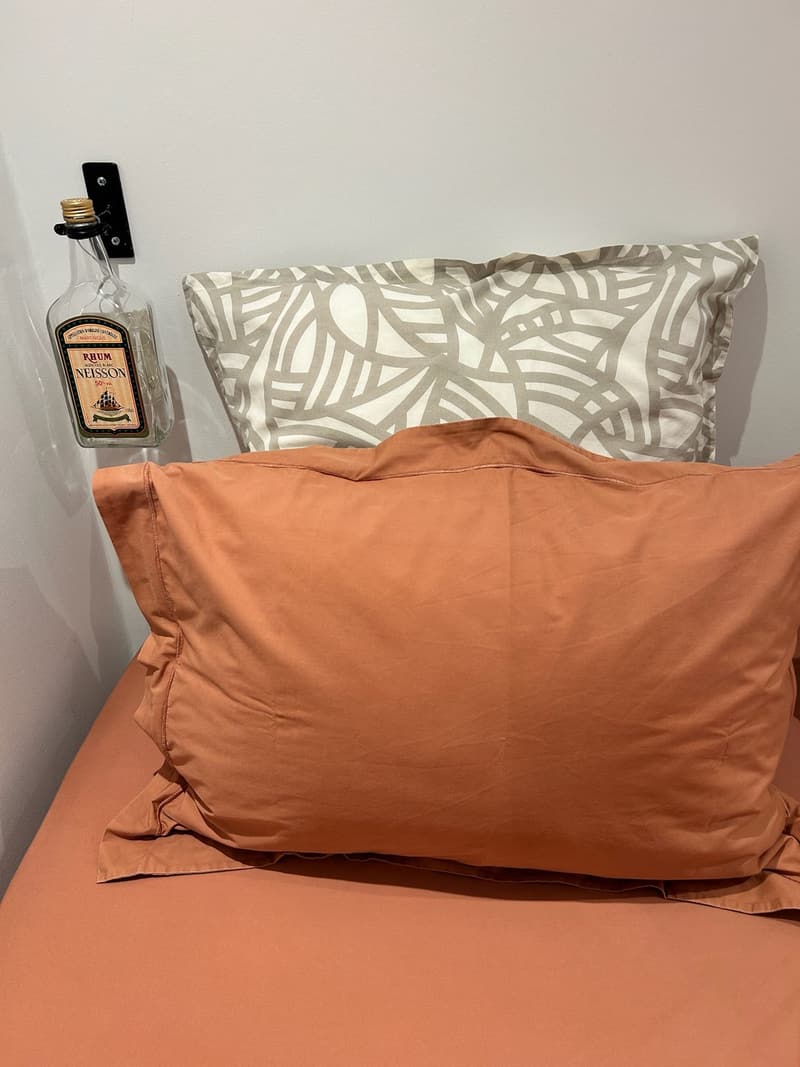 Le lit de la chambre, linge corail et coussins imprimés