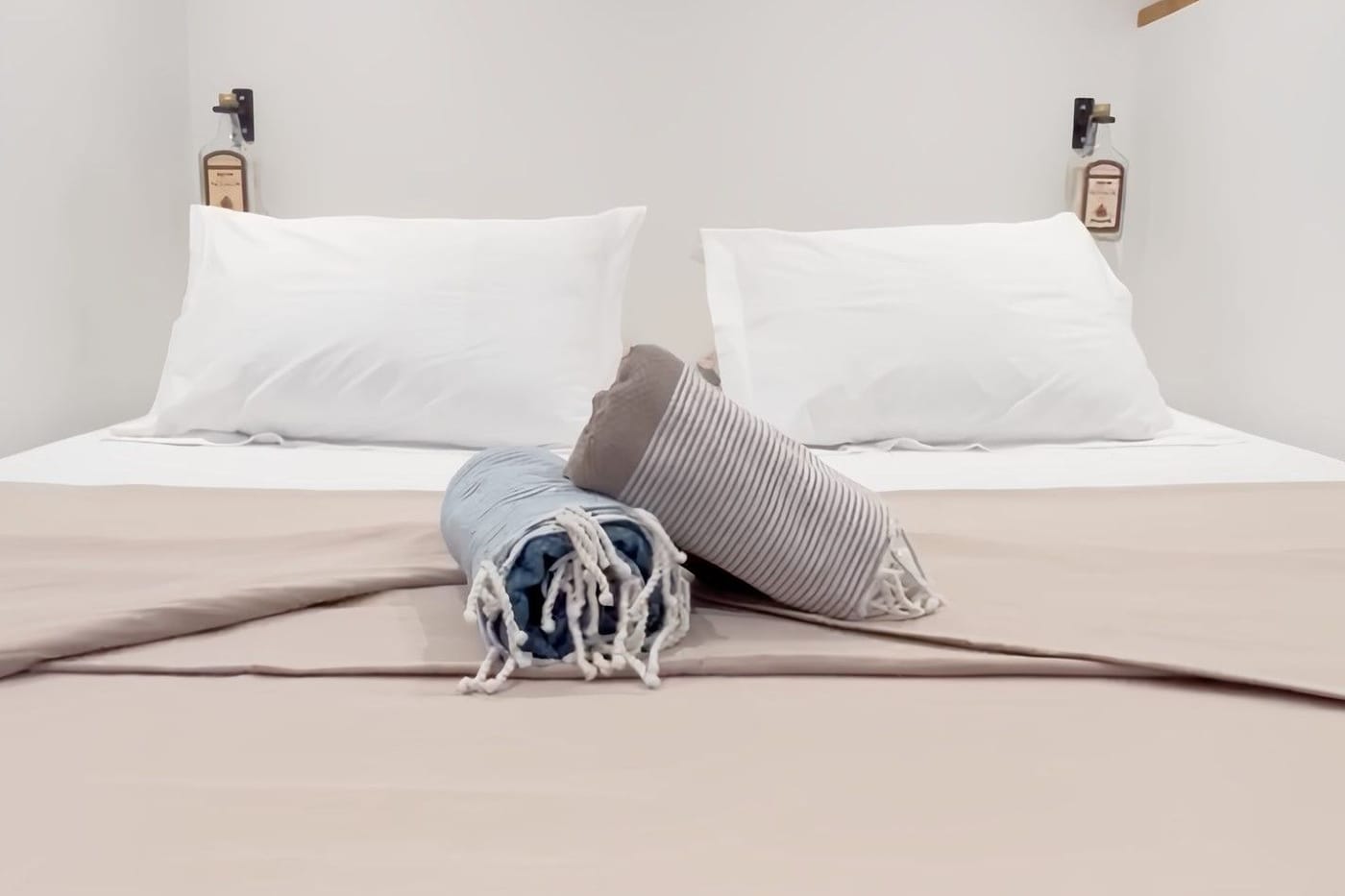 The bedroom: the king-size bed with white sheets, two pillows and rolled foutas